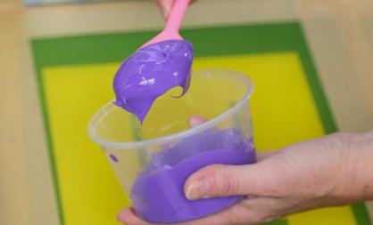 Hand holding a plastic container with purple ink and a pink spoon