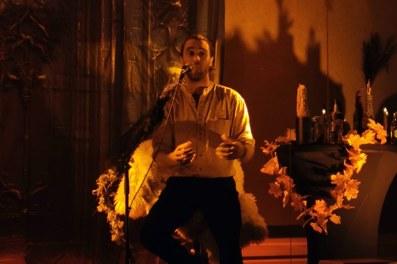 Man on stage singing/talking in candlelit lighting