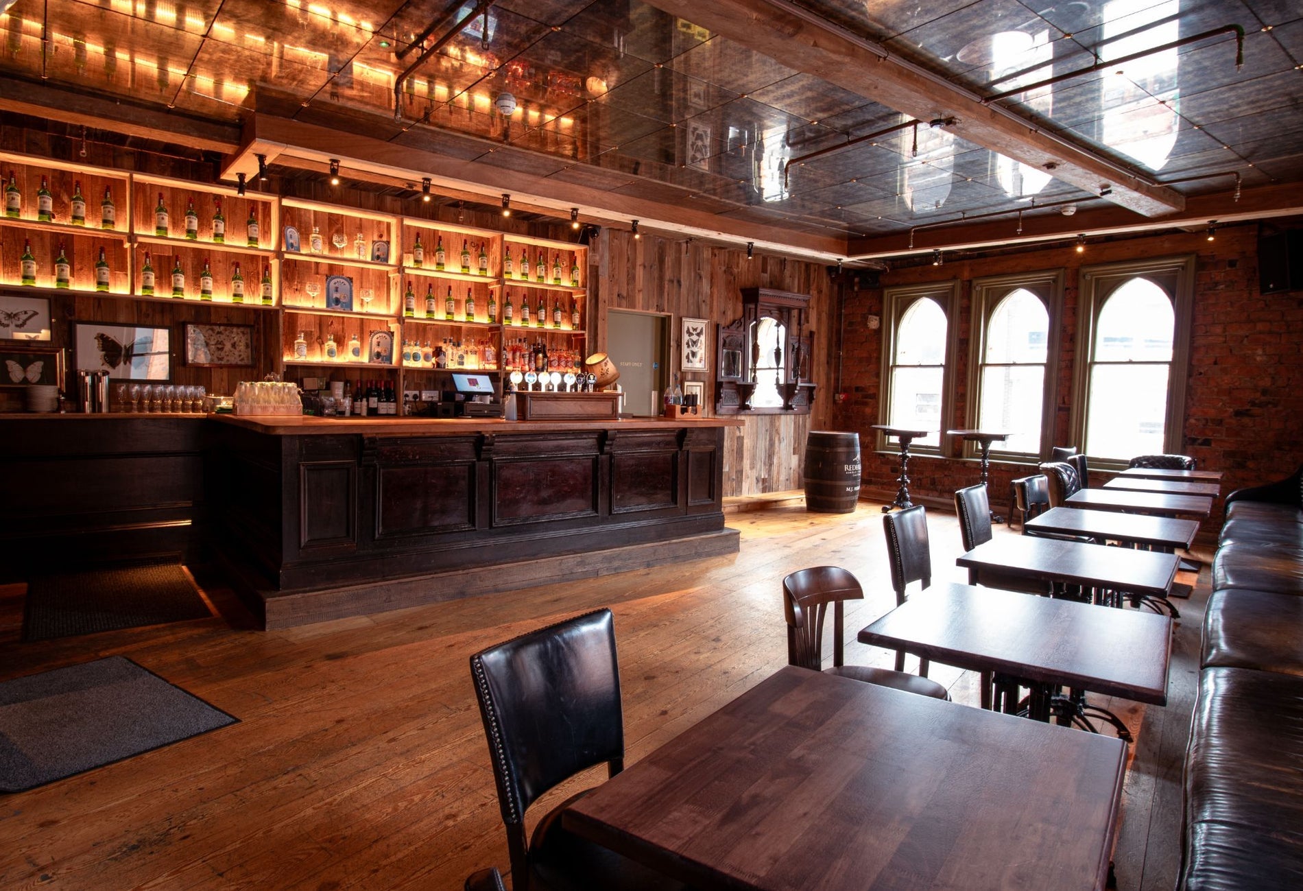Interior of a traditional pub featuring a wooden bar with exposed brick walls and large arched windows