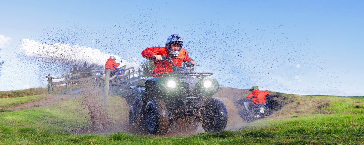 A man on a quad bike driving through a muddy field with mud spray visible in the image