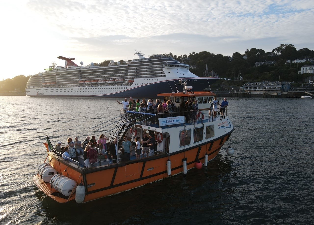 A boat with passengers in a harbour with a large cruise ship in the background
