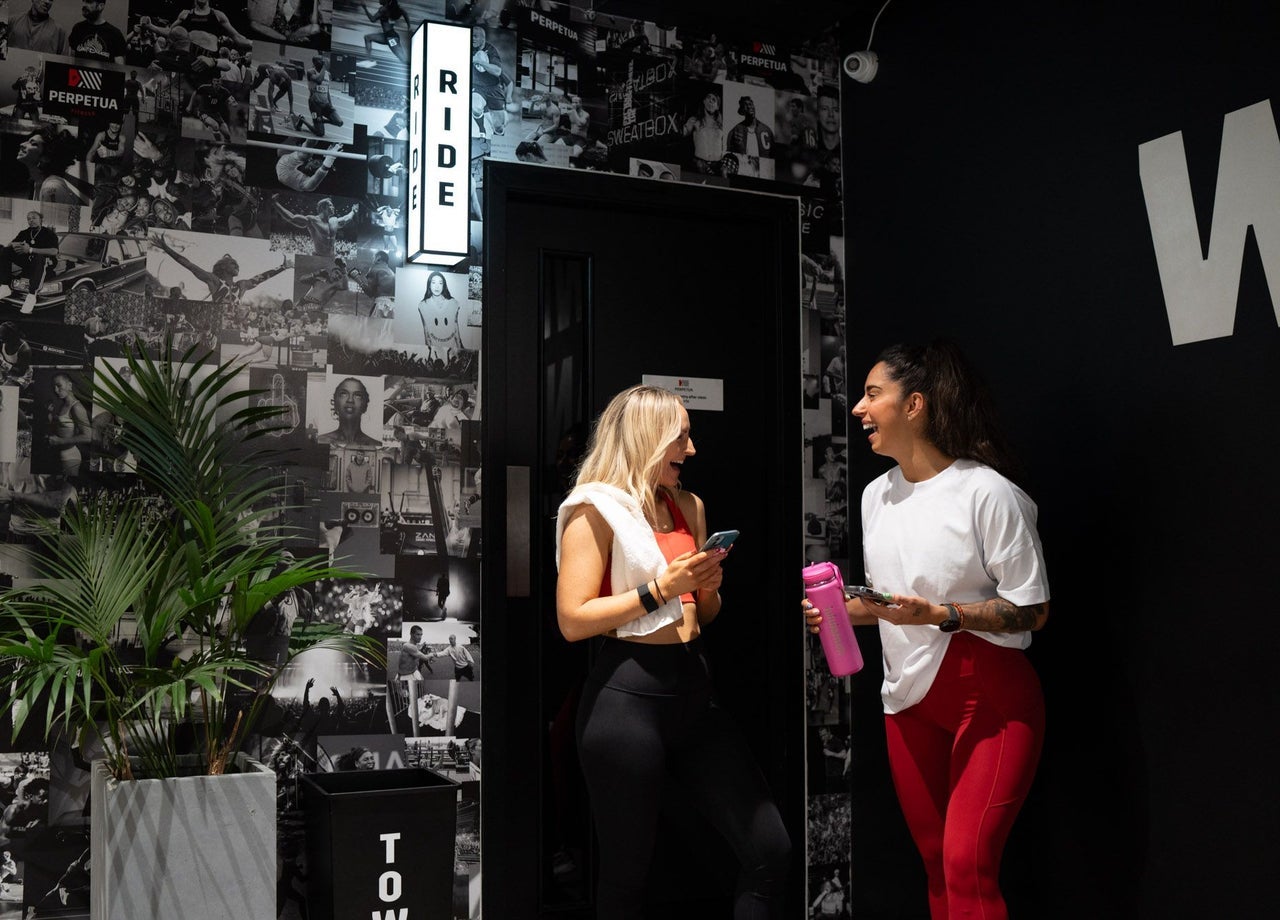 Gym members chatting against a dark wall of fitness imagery