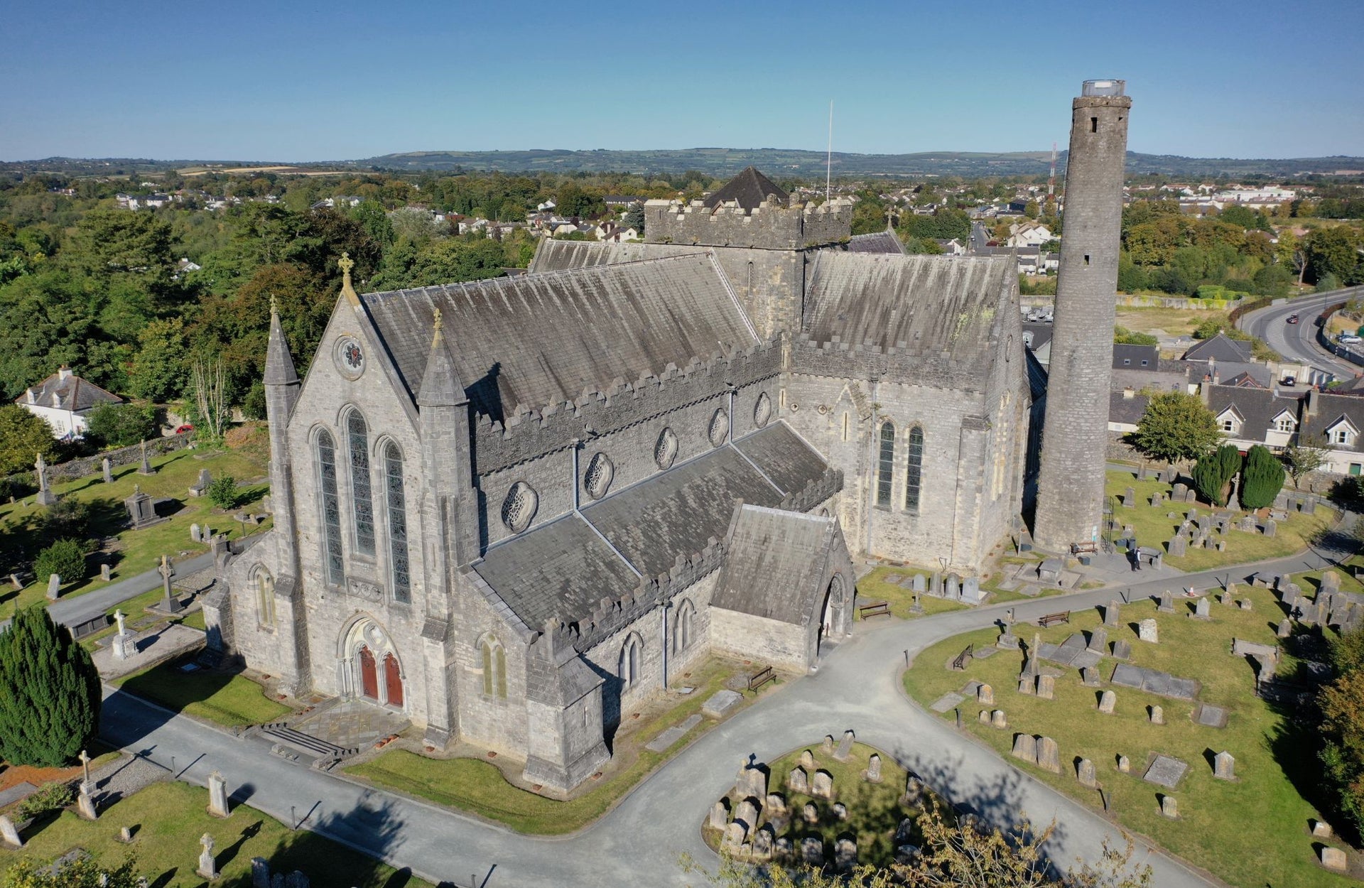 An aerial view of a cathedral building with a round tower beside it surrounded by grave stones