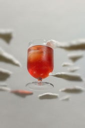Looking up at an orange coloured cocktail in a short glass from beneath a glass surface