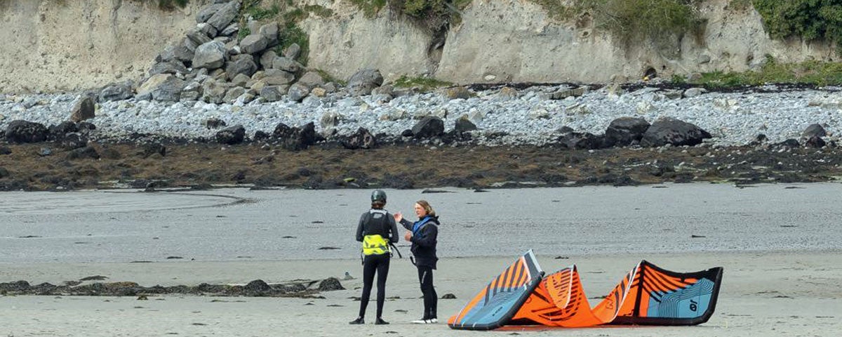 Two people on beach with orange and blue kite next to them