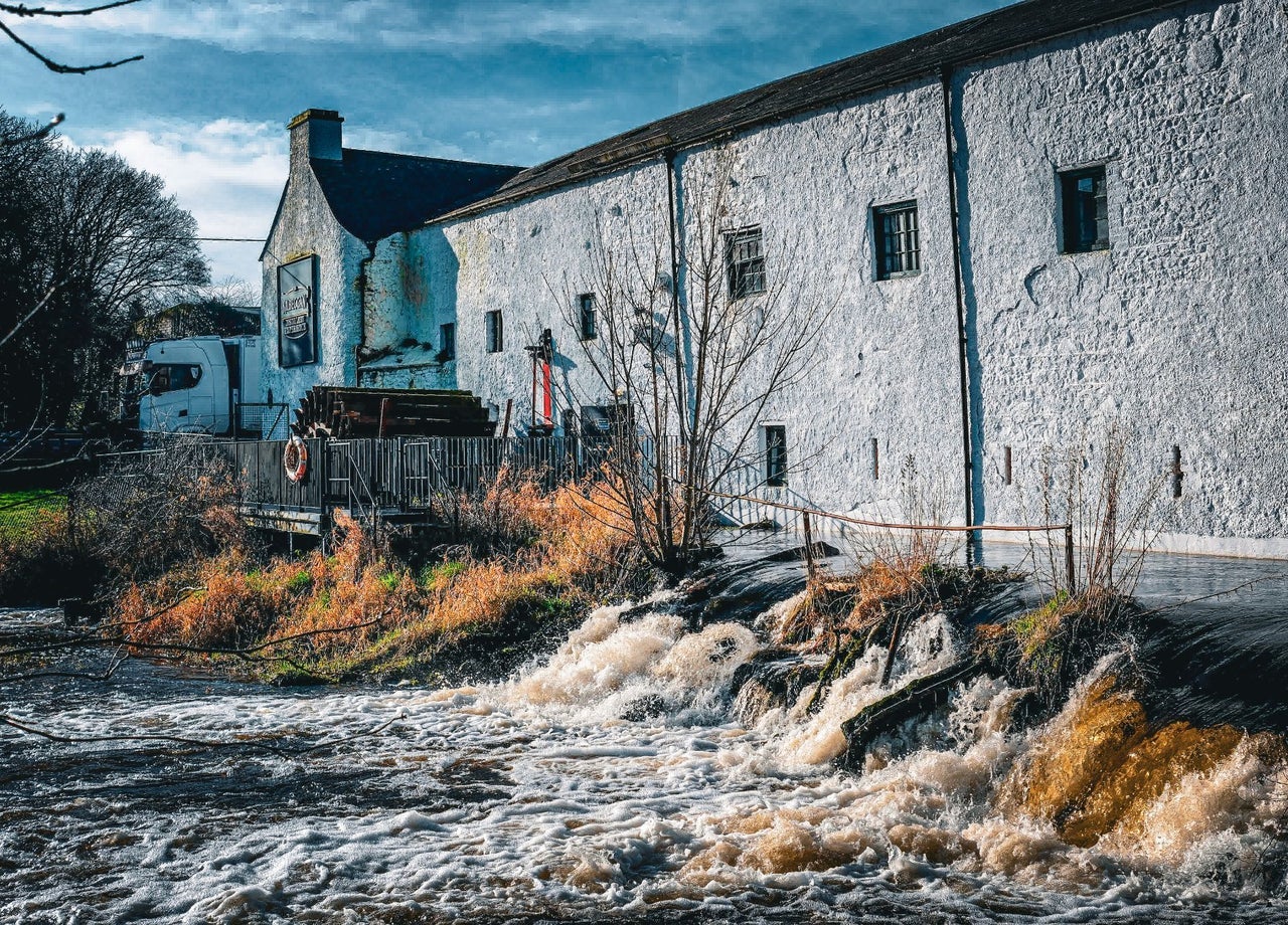 Historic whitewashed distillery buildings standing beside a flowing river
