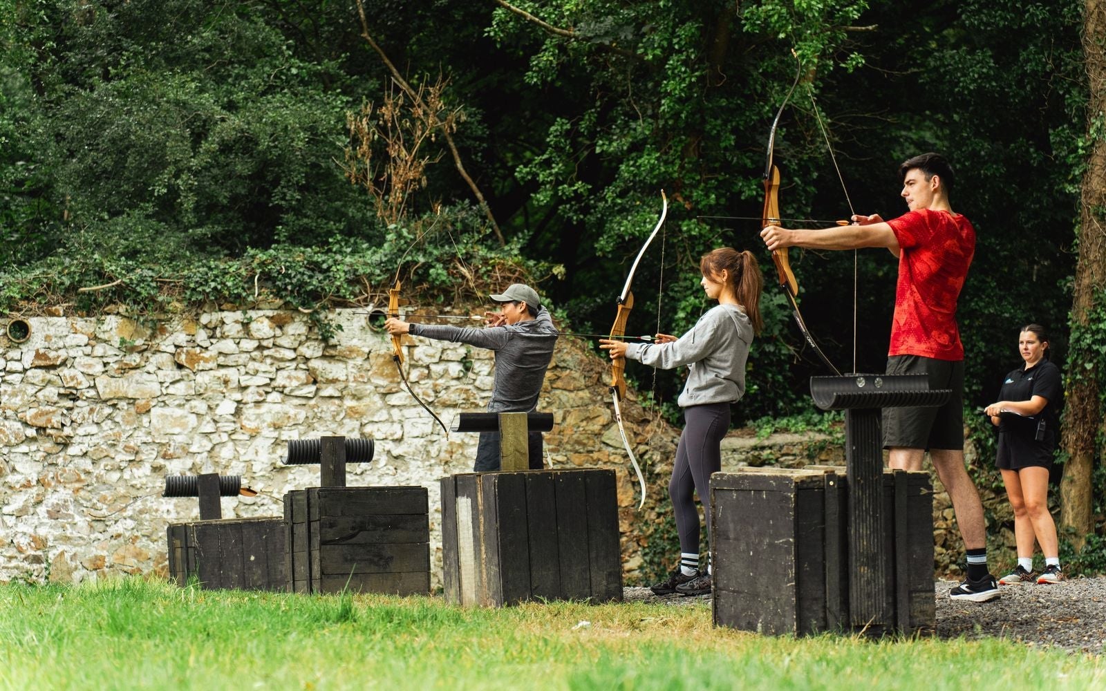 Three people practice archery with an instructor standing behind them