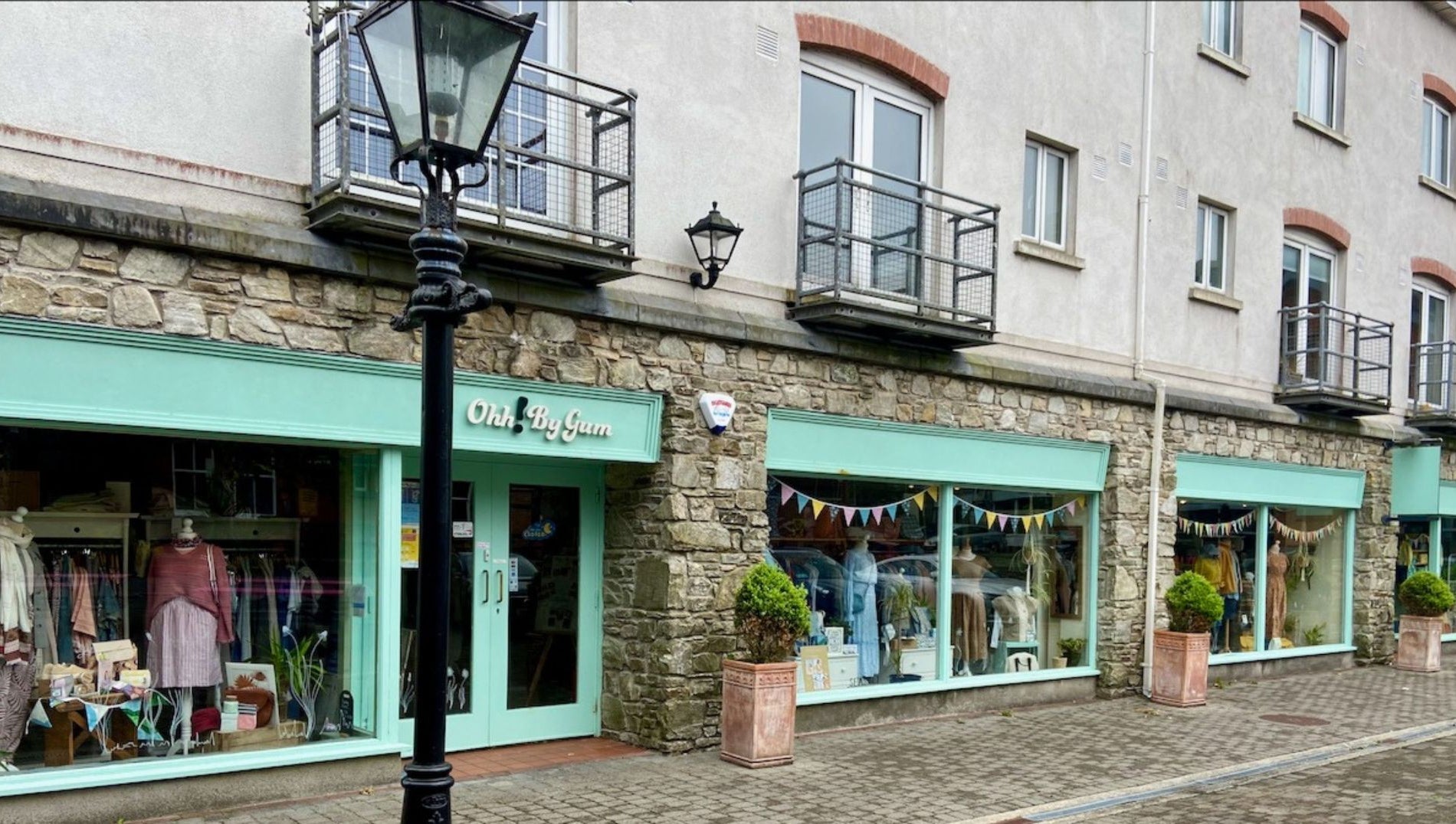 Shop front with mint green window and door frames and planters in front and a black lamp post on the street