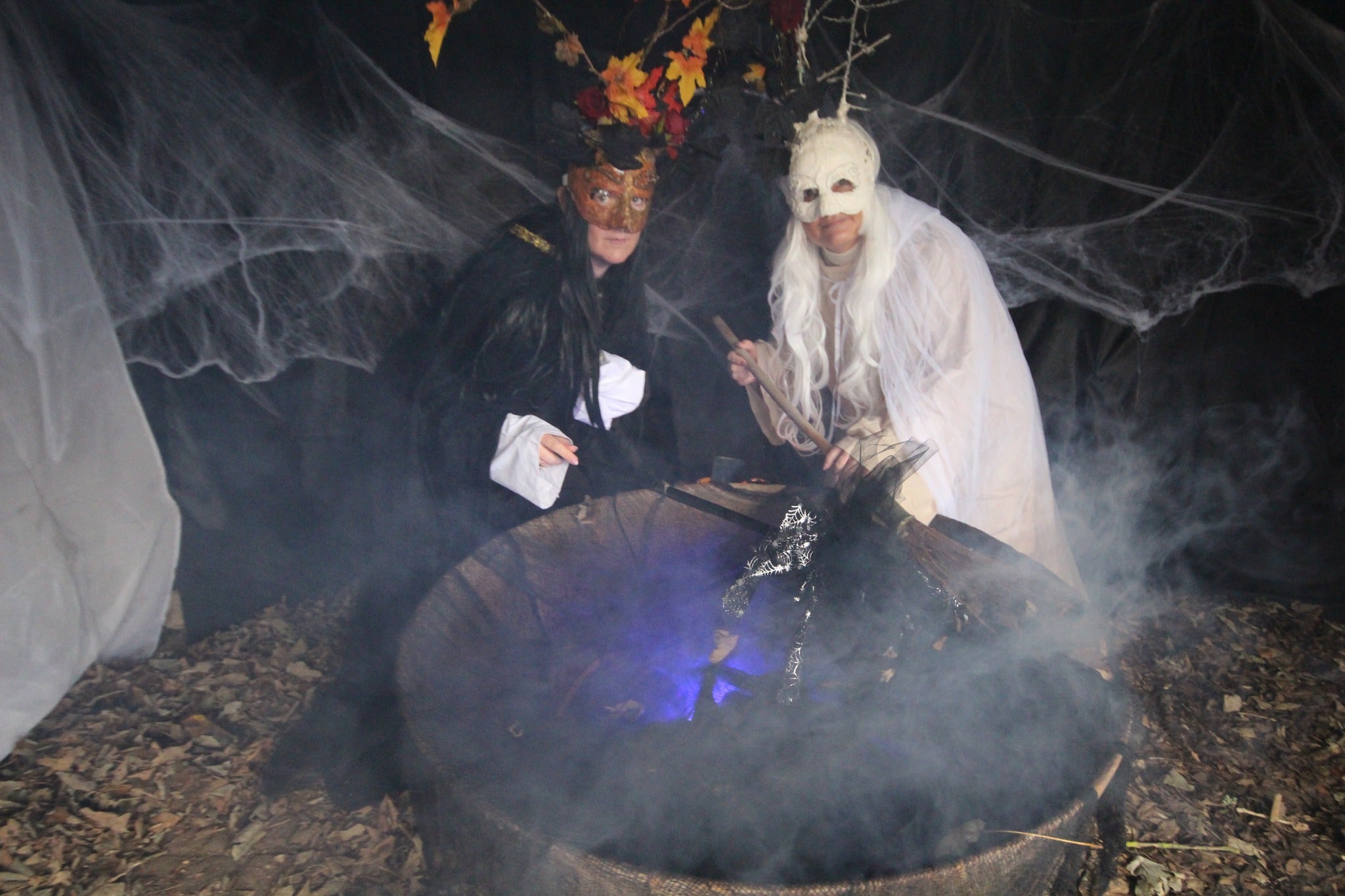 two people, one in white and one in black over a cauldron mixing it up
