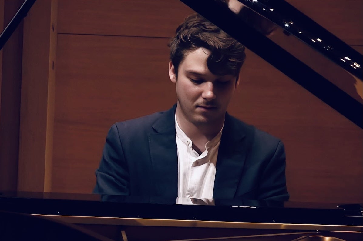 A man looking down at keyboard, seated at a grand piano