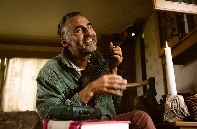 A smiling man seated in a chair with a tall lit candle