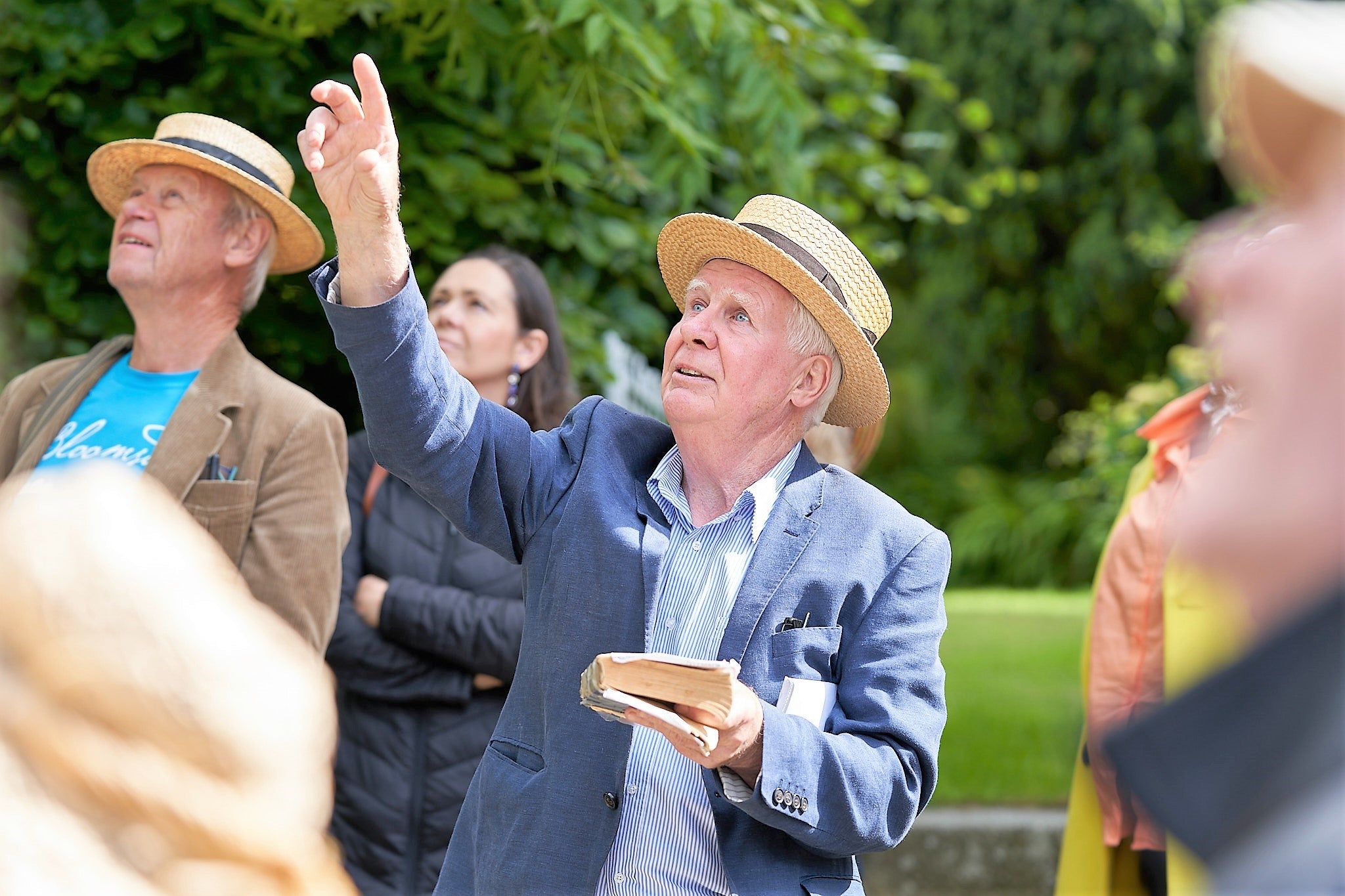 A small group of people looking upwards outdoors with central man pointing upwards.