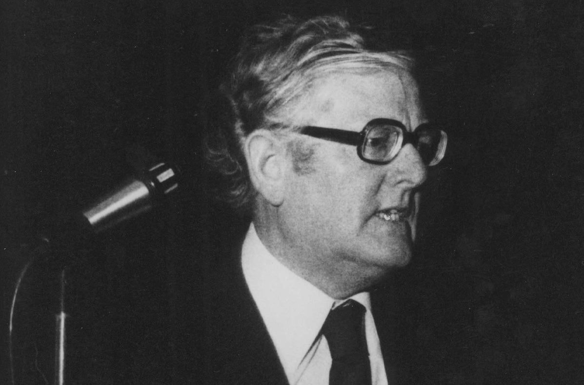 Old black and white, slightly grainy photo of man in suit and tie giving a speech