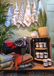A selection of coloured handmade throws and scarves on display with homemade jars of chutney and jams