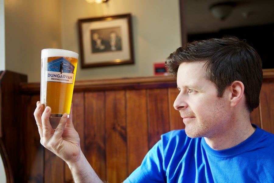 A man holds a pint of Dungarvan Brewery beer up to the light