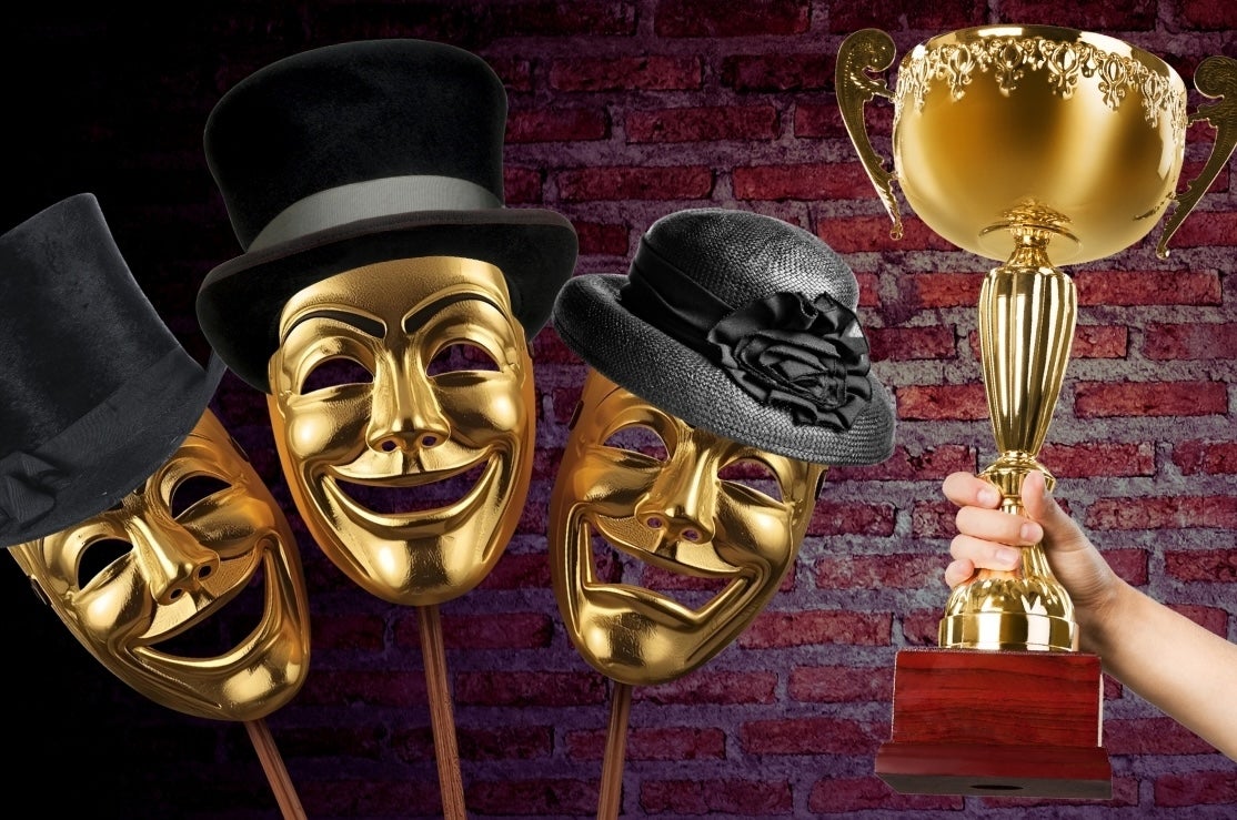 3 gold face masks laughing or crying wearing black formal hats beside hand holding up a large gold trophy