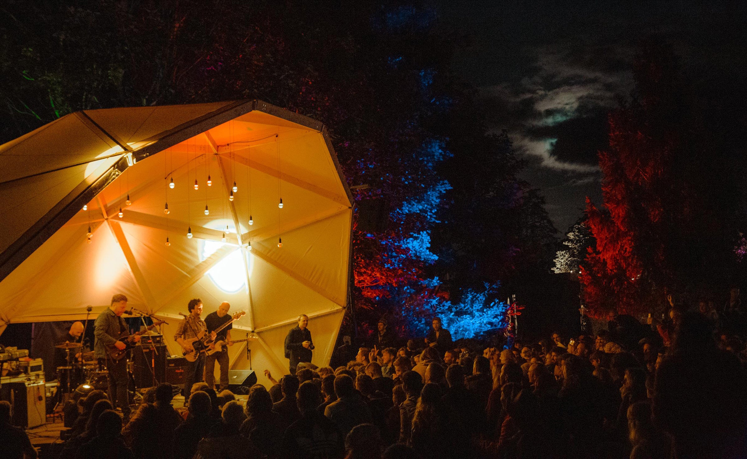 Audience surrounding a lit stage at an evening performance - Another Love Story festival.