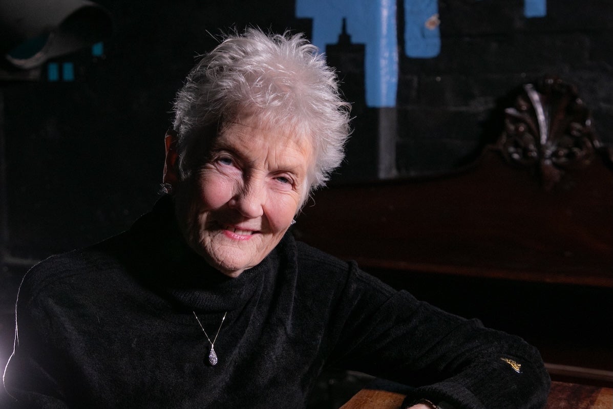 A smiling elderly woman in dark jumper