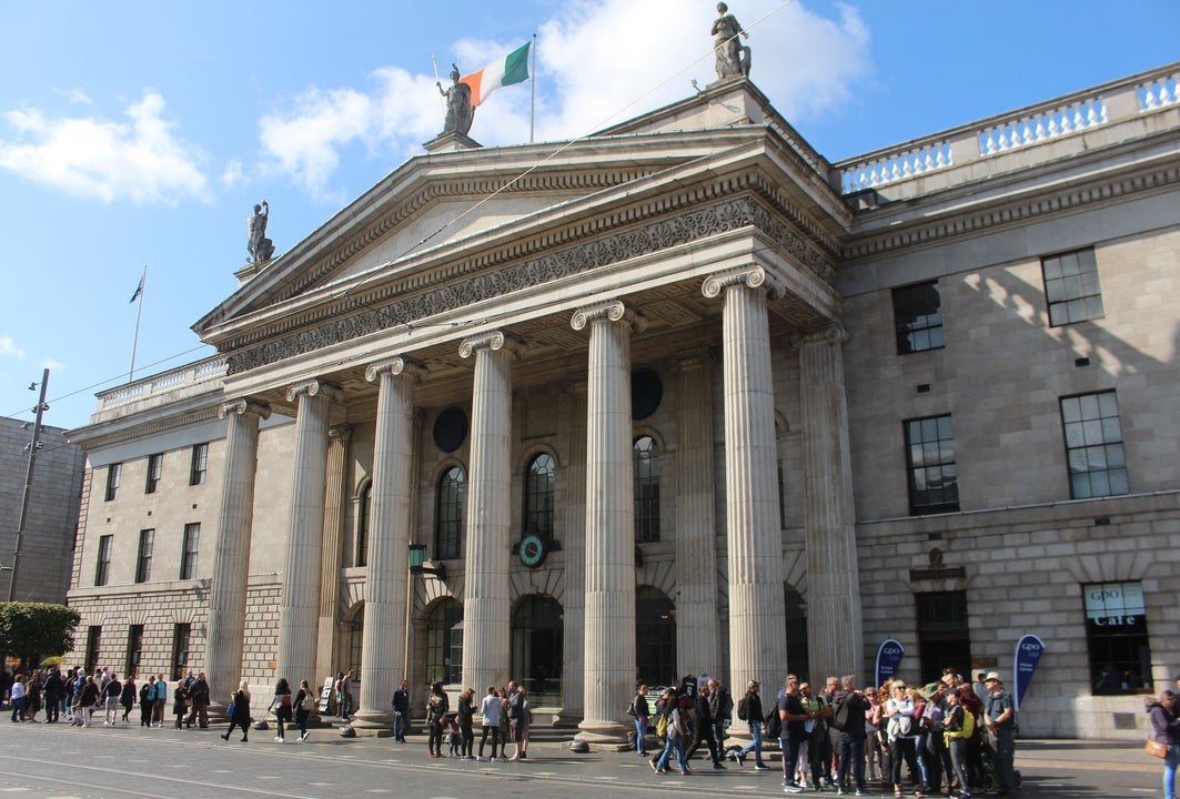 A walking tour group and guide outside a stately building on a busy city street
