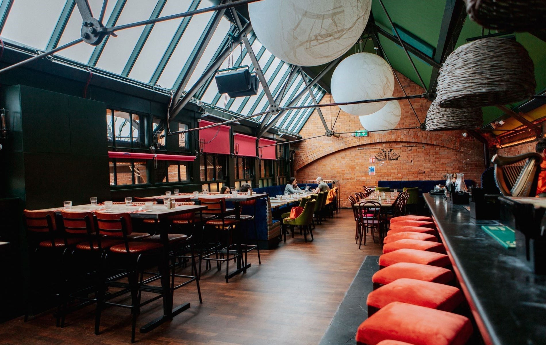 Bar area with exposed brick walls skylights red seating and large pendant lights above the tables