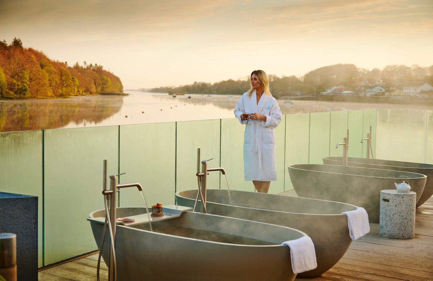 Woman in an Ice House Hotel bathrobe leaning on the glass railing overlooking the water in Ballina standing beside seaweed baths.