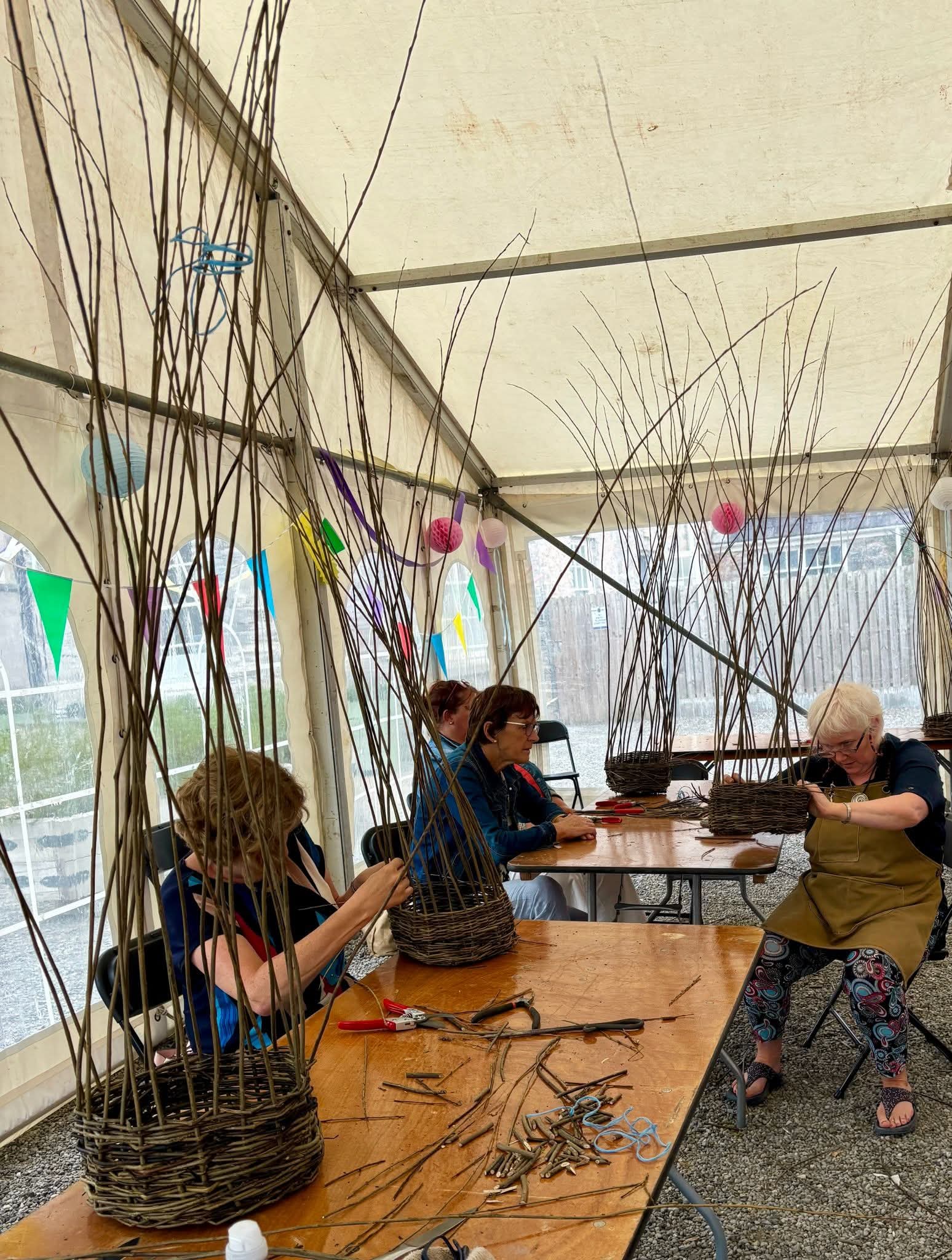 People seated at tables weaving baskets with tail willow canes 