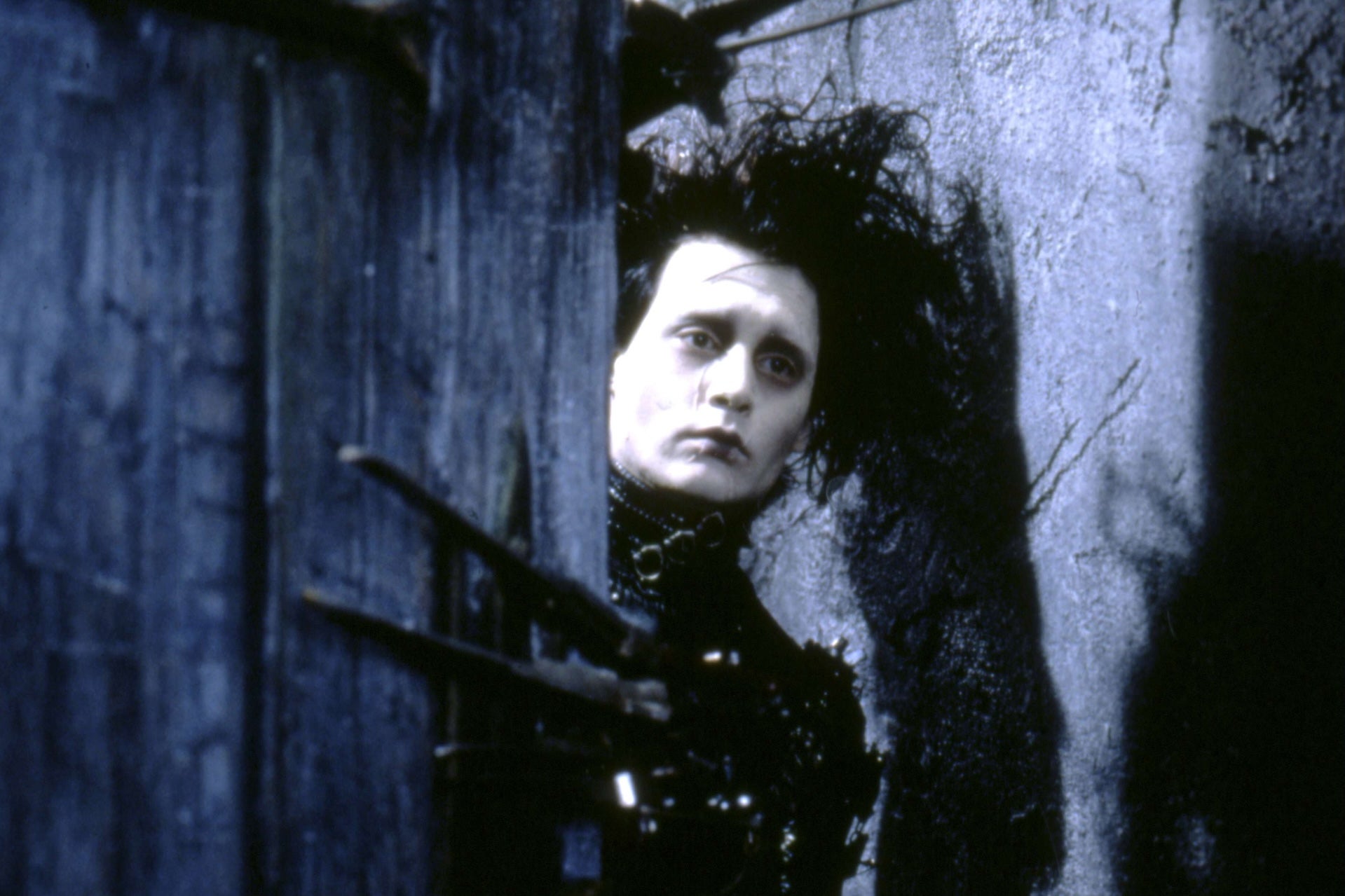 Edward Scissorhands is holding open a door. His has a sad expression.