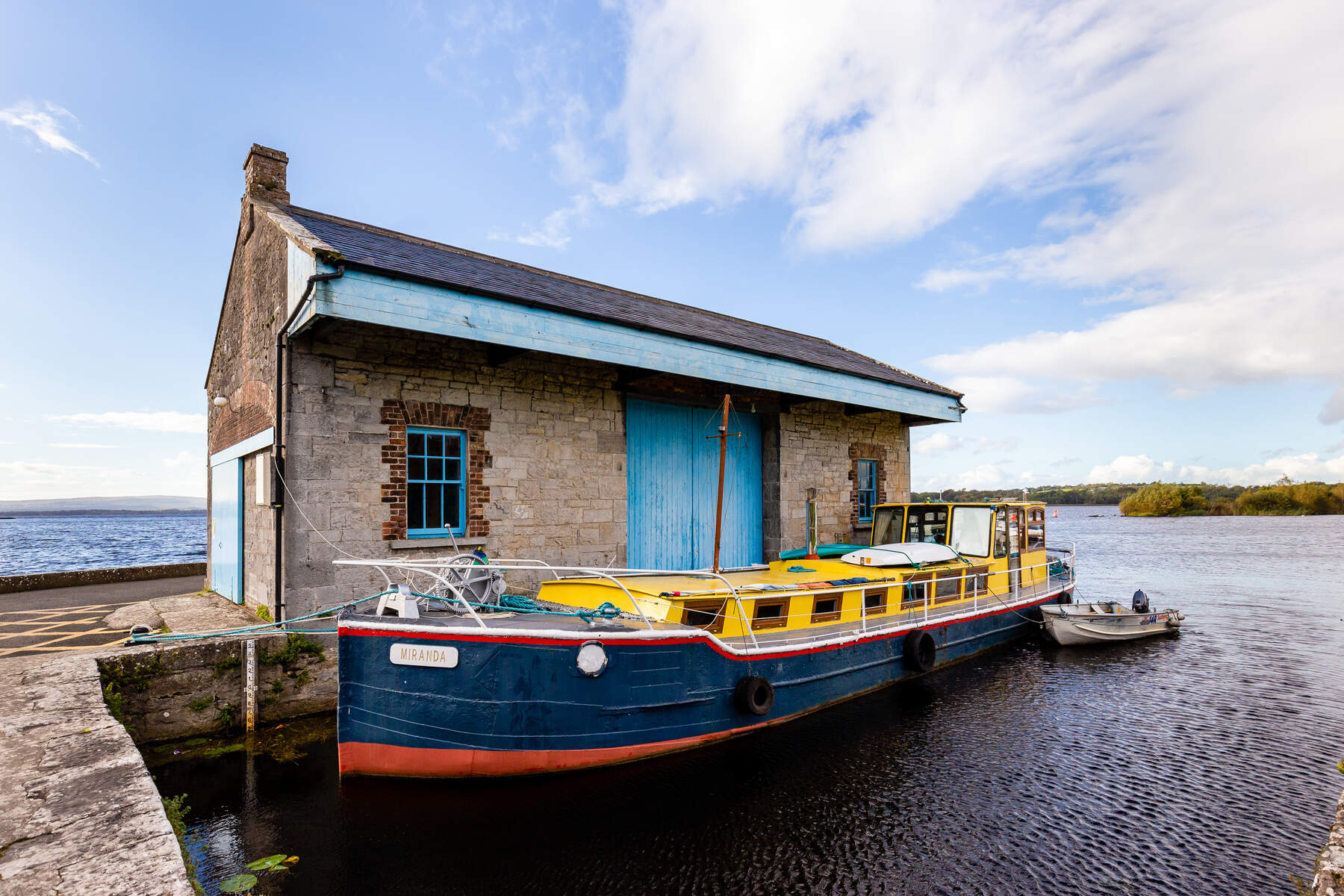 Yellow and navy boat moored outside a boat house with a blue door