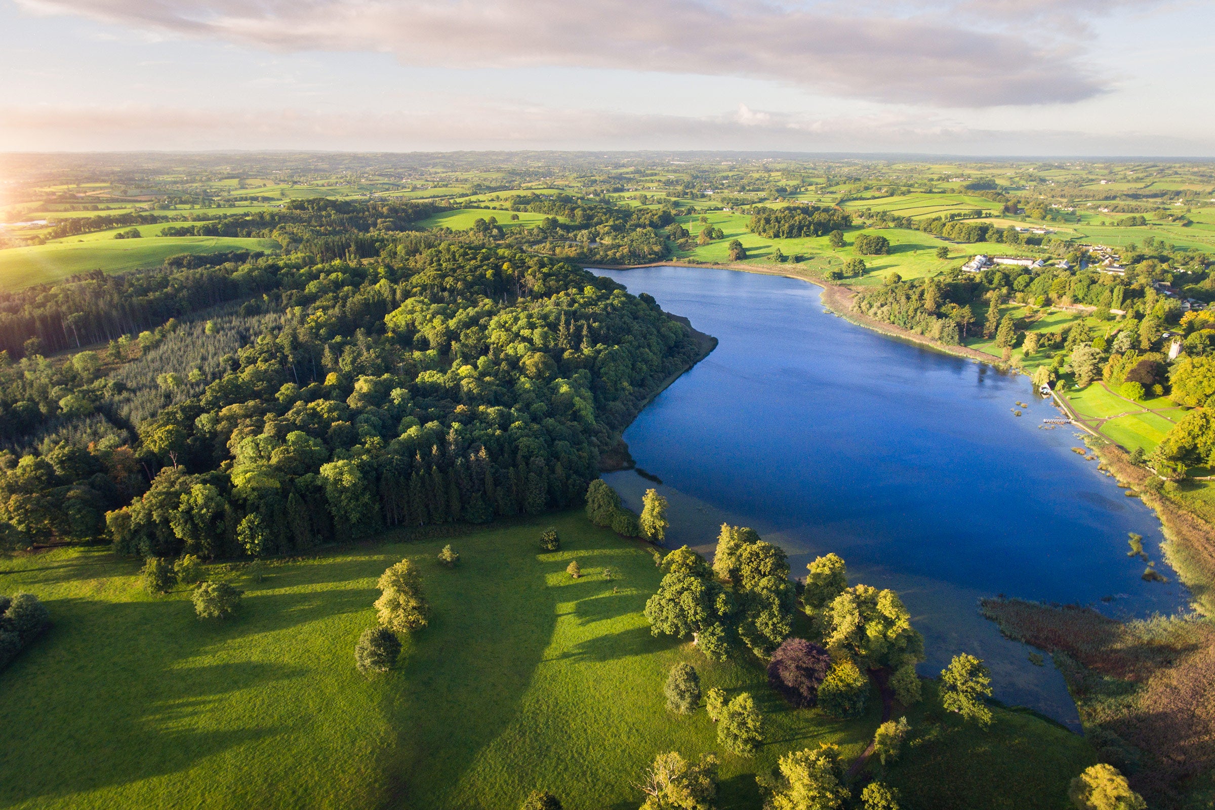 Aerial view of lush green landscapes and a clear blue lake at Castle Leslie Estate