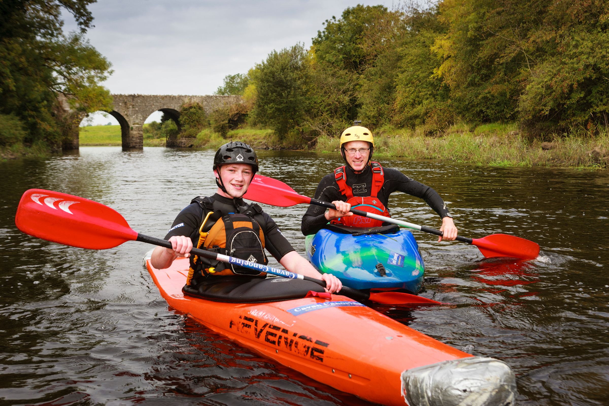 Two people in orange boats kayaking down a river.