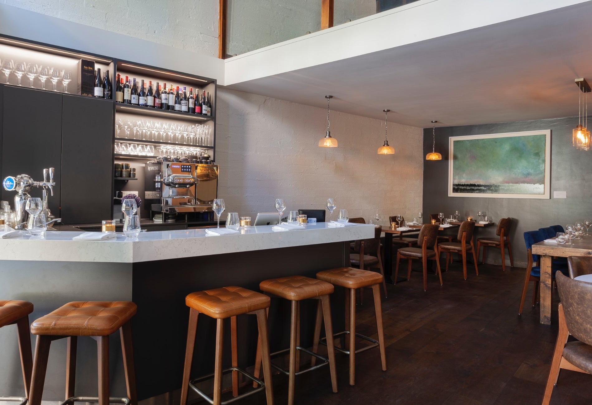 Interior of a bar setting with bar stools at the counter and tables set for service