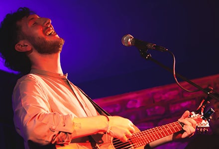 A man singing with head thrown back, playing a guitar.