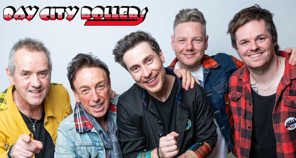 A group of smiling men of various ages, some wearing checked red and black tartan.