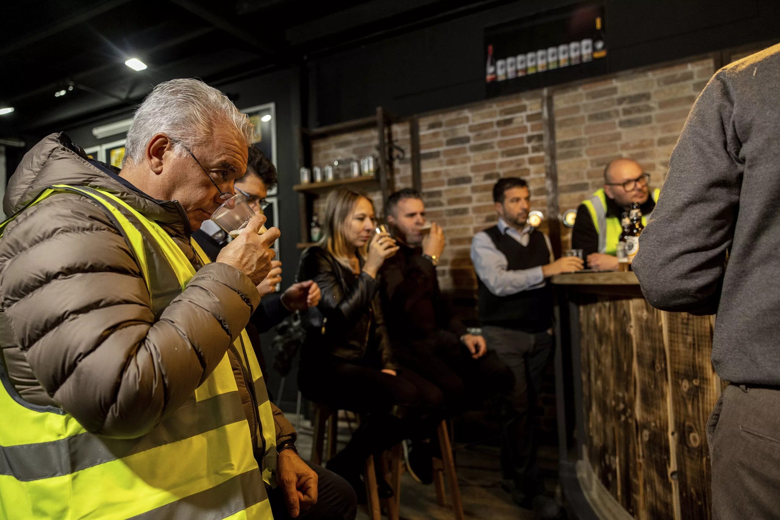 A group of people drinking from a small glass on a brewery tour.