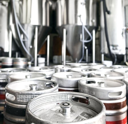Silver kegs some with a red and a brown stripe in a brewery room