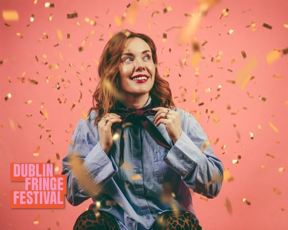 Sadhbh McLoughlin stands in front of a pink background with gold confetti falling around her.