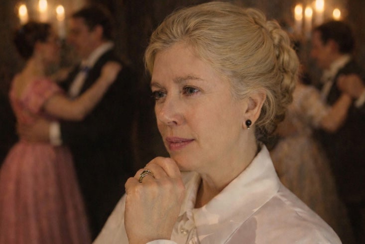 A thoughtful looking woman in white blouse with couples dancing in background lit by candles.
