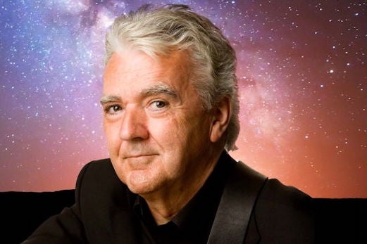 A smiling man against dark blue, purple and orange starry sky