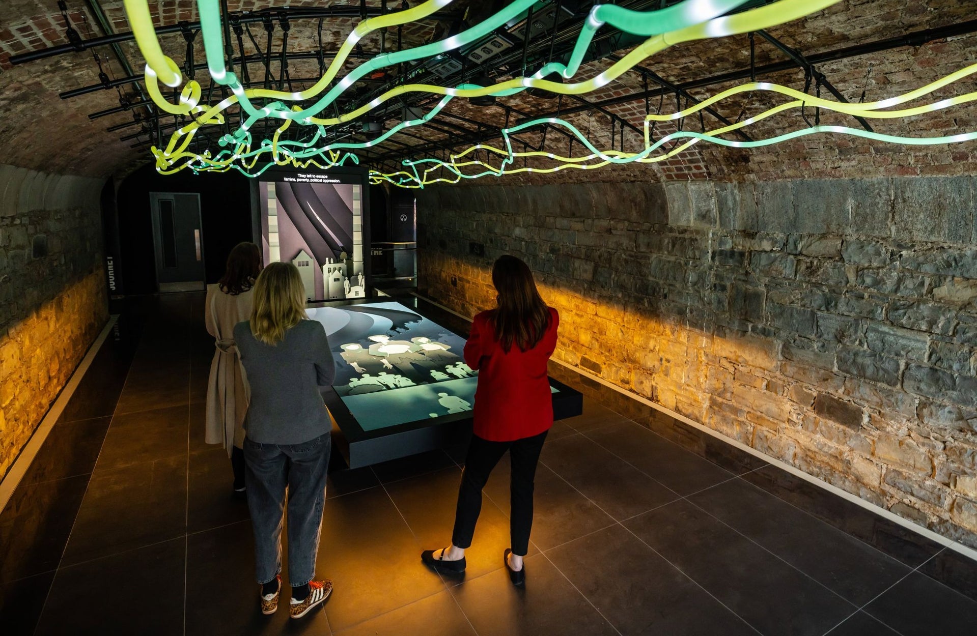 An interactive display table in a stone vaulted room with illuminated rope lighting along the ceiling