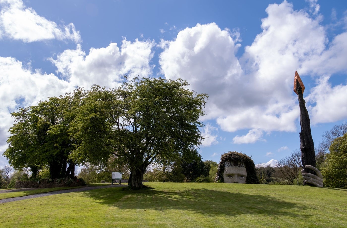 Green field with a giant head poking up from the ground holding a very tall spear