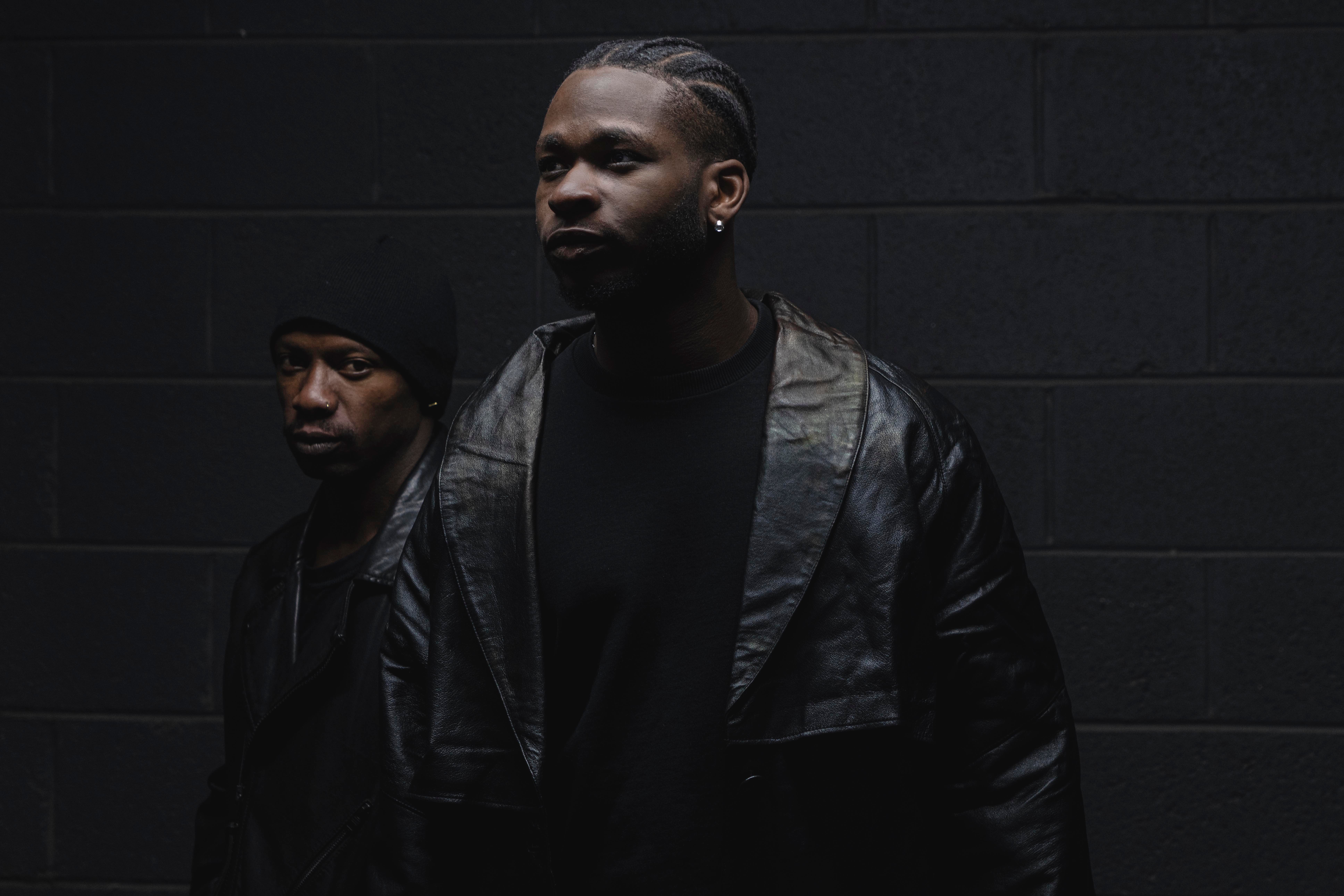 Very darkly lit photo of 2 men in dark clothing so barely visible.