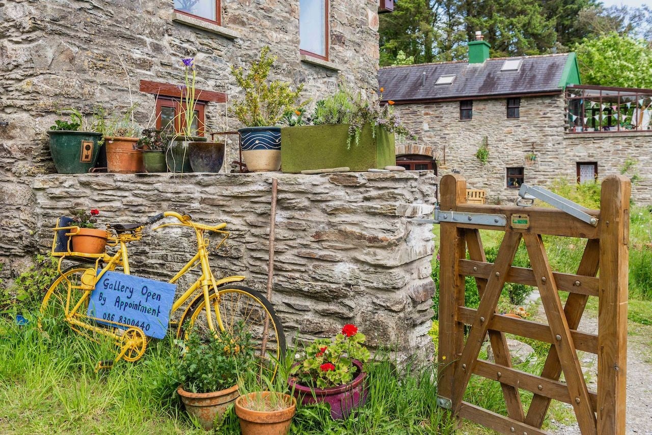 A stone wall with colourful plants and a large stone farm building in the background