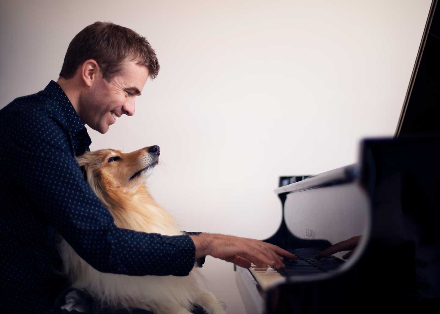Fiachra Garvey piano recital Thomastown Concert Hall 8 February 2026 - side view of a smiling man seated at piano keyboard with dog on his lap