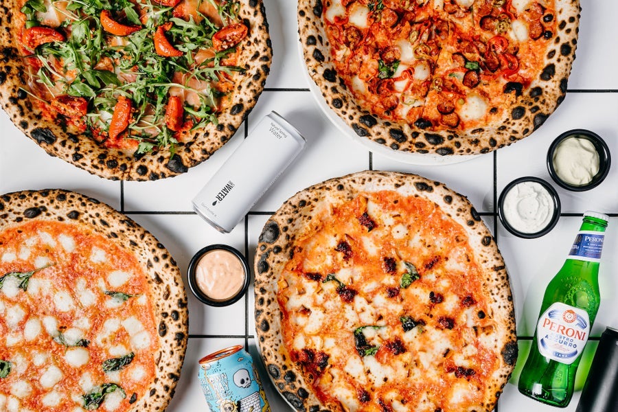 Four pizzas on a table with dips and drinks