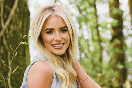 A smiling woman with blurry trees in the background.