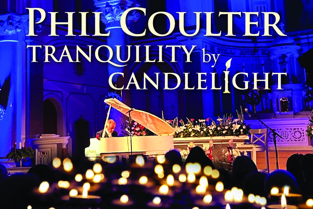 A man in the background playing a pale coloured grand piano with blurry lit candles in the foreground.