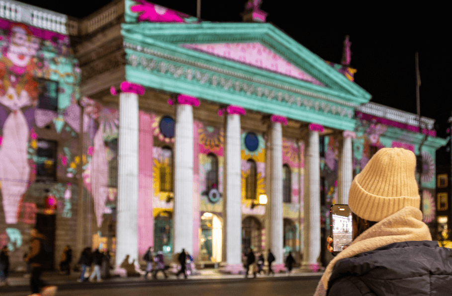 Brigit 2026: Illuminating the GPO - view of a large building with tall columns at night covered in light show with rear view of person looking on.