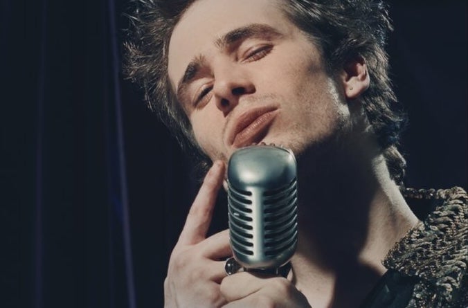 A man singing into large old style mic with eyes shut.