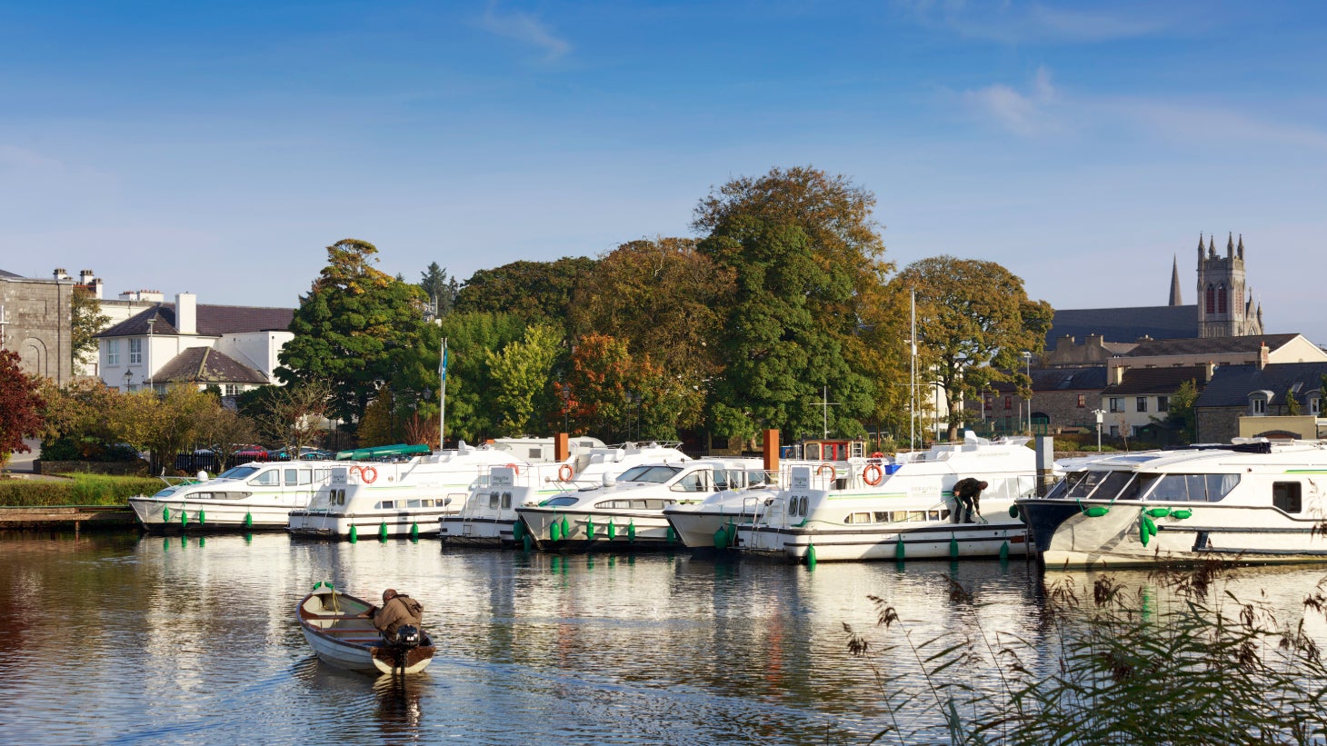 Boats in a marina with a backdrop of trees and a church in Carrick-on-Shannon, Leitrim