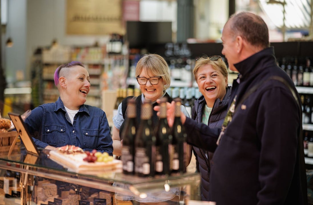 Four people standing at a counter with wine and food on it